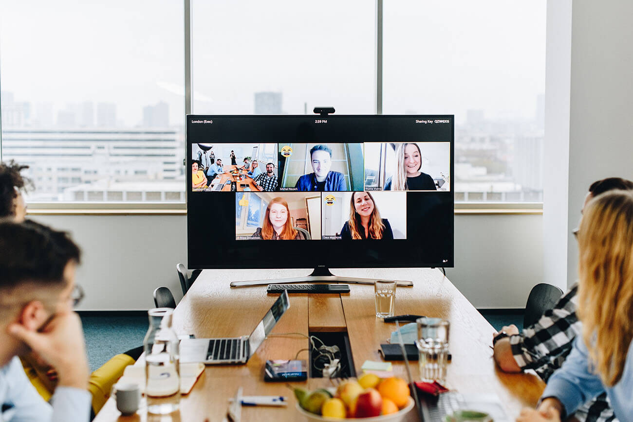 colleagues sitting behind a desk during a meeting while the rest of the team joins remotely